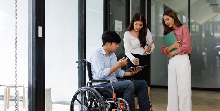 Group shot of diverse business people, disabled asian man on wheelchair chatting with colleagues together at meeting room at office
