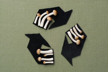 Creative recycling symbol with fresh mushrooms on a green textile background. Environmentally friendly alternative to synthetic fibers in the textile industry. Future of ethical fashion.