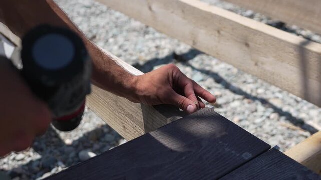 Building Decking Screw Hand fastening dark composite board onto wooden frame outdoor project