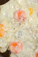 A close-up shot of multiple fried eggs with sprinkled pepper sizzling in a pan