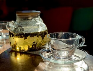 Transparent teapot with milk oolong leaves brewing, glass cup on the table. Cafe creates a cozy tea ceremony and lifestyle mood
