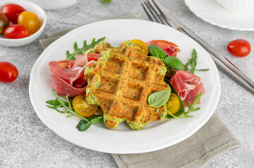 Spinach waffles with tomatoes, arugula and prosciutto on a white plate with a cup of coffee. Healthy breakfast. Top view