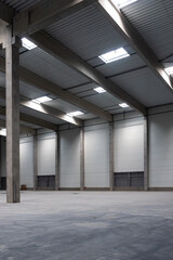 The empty interior of a large industrial warehouse. The concrete industrial hall is flooded with natural light.