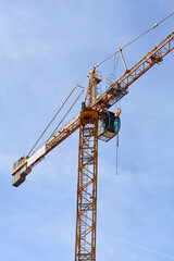 A low-angle shot of a large yellow construction crane with a cabin and counterweights against a clear blue sky