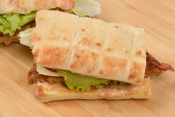 A top-down shot of two flatbread sandwiches with a hamburger patty and fresh lettuce on a wooden board