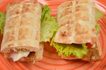 A horizontal close-up shot of two flatbread sandwiches with a hamburger patty and fresh lettuce on an orange plate