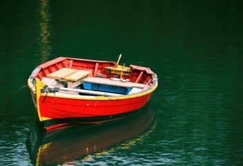 Obraz premium Red Wooden Rowboat on Calm Green Water.