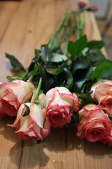 Fototapeta premium Bouquet of delicate pink and white roses with green leaves, elegantly arranged on a wooden surface. Perfect for advertising romantic themes, wedding decorations, greeting cards, or gift promotions.