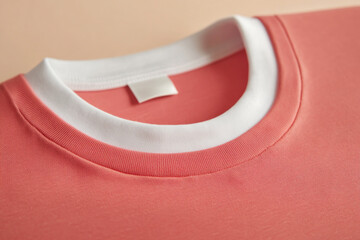 Closeup of a salmoncolored tshirt with a white collar and a small tag, showcasing the texture and design details against a neutral backdrop