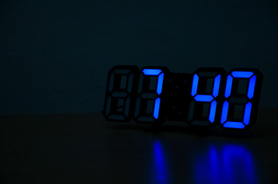 A close-up shot of a modern digital clock with glowing blue LED numbers showing the time 07:40, set against a dark background, highlighting the concept of time, technology, and the night. - Powered by Adobe