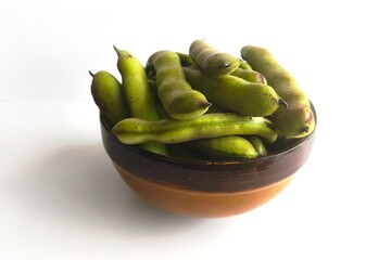 Fresh broad beans in green pods placed in a rustic clay bowl on a white background. Top view of healthy legumes, perfect for cooking and gardening.