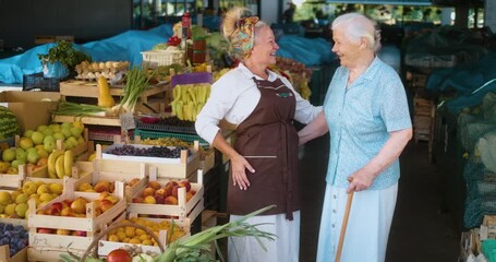 Active retired grandmother at farmers market buying groceries, chatting and laughing with friendly female vendor, concept of joyful aging, social connection, and healthy lifestyle. - Powered by Adobe
