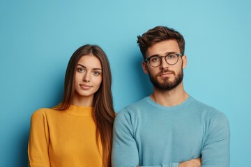 Obraz premium Young couple poses casually against a bright blue wall wearing colorful sweaters and glasses