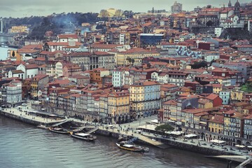 Obraz premium Views of the Ribeira district in Porto, Portugal on a cloudy day. People stroll along the river Douro and traditional boats are moored at the quayside