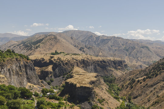 View of rugged cliffs dropping into a lush valley, under a vast sky, contrasting textures and hues across the terrain, Garni, Kotayk Province, Armenia.