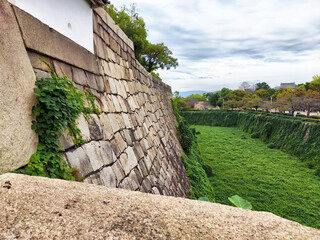 Historical stone wall surrounds lush green moat, offering tranquility and nature's beauty by the old fortress
