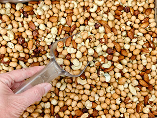 Various types of nuts in bulk displayed with a hand holding a scoop