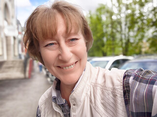 Mature blonde woman enjoying a selfie during a lively trip in a charming neighborhood