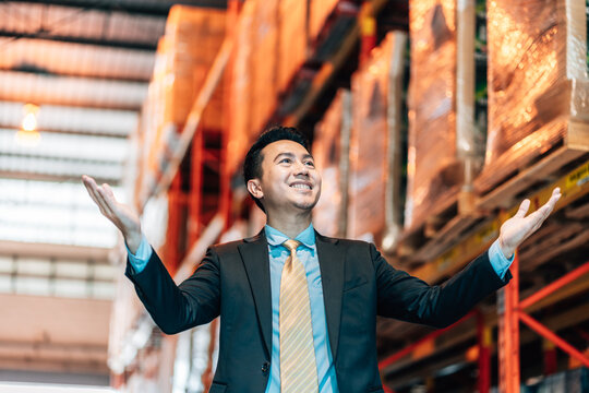 businessman in a suit stands in a warehouse with his arms outstretched, smiling up at the stocked shelves.