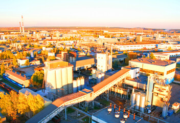Industry Operations Across a Sprawling Factory Complex During Sunset, aerial view. View captures large industrial complex with ready mix concrete under warm sunset sky. Cement plant, drone view.