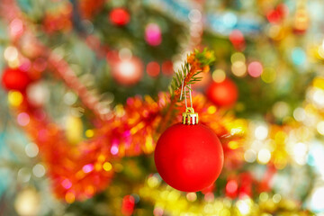 Bright Red Ornament Hanging on Christmas Tree With Colorful Decorations in Festive Setting. Vibrant red ball, ornament dangles on fir-tree. Christmas tree adorned with shiny lights in New Year.