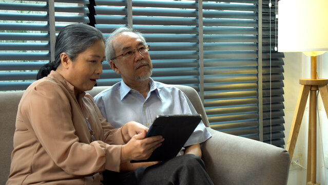 Grandmother pointing finger touchscreen picture on digital tablet for husband Alzheimer’s pain sitting together sofa at home.Elderly couple  memory disability patient health support care. Family care - Powered by Adobe