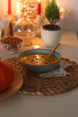 Plate of pumpkin soup, pumpkins, glass of wine, nuts and lit candles on the table. Selective focus.
