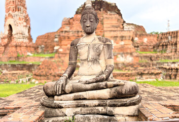 Fototapeta premium Ancient stone Buddha statue in meditation pose at historic temple ruins, Ayutthaya, Thailand, cultural heritage site and UNESCO world landmark with weathered brick architecture in the background.