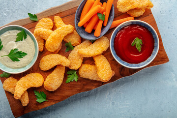 Chicken nuggets with fresh vegetables and dips, on a wooden board, shot from above with a place for text