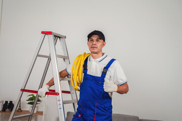 Professional male technician in uniform standing confidently with ladder and tools providing maintenance service in modern interior space
