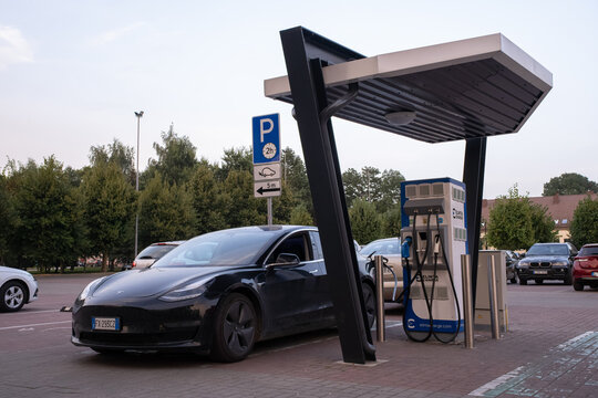 Marijampole, Lithuania - August 24, 2022: A static shot of a solid black Tesla Model 3 dual motor charging at the Elinta DC in a cloudy summer day. Selective focus.