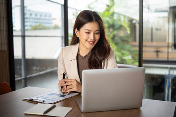 Fototapeta premium Confident businesswoman smiling while working on her laptop in a modern office.