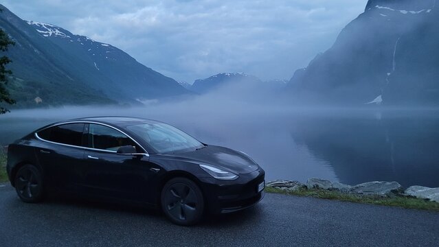 Hyen, Norway - Jun 26, 2022: Wonderful landscapes on the road in Norway. Hyen surroundings scenic view at midnight. A static shot of a Tesla Model 3. Fjord in the fog. Selective focus