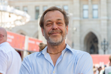 Portrait of a middle-aged man with a beard against the background of urban architecture and people.