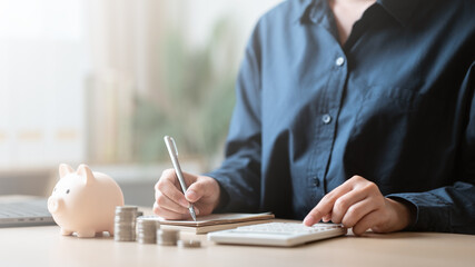Person writing and calculating with coins, piggy bank, and notebook, representing lifestyle finance