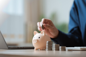 Hand putting coin into piggy bank with stacked coins, symbolizing lifestyle finance, saving money.