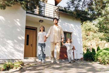 Happy family, positive father and little daughters walking out of their modern house on sunny day