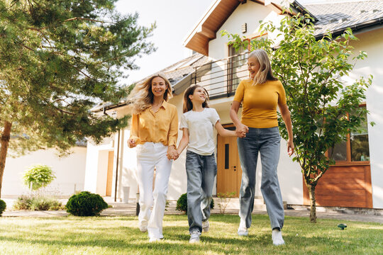 Happy family walking together in front of house beautiful mother grandmother and little girl