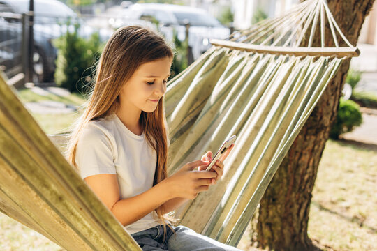 Smiling happy girl relaxing in hammock using smartphone on sunny day - Powered by Adobe