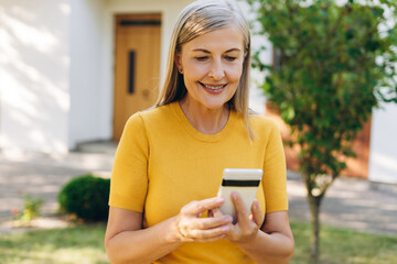 Smiling senior woman holding mobile phone using mobile phone in front of house