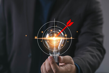 Businessman holding glowing light bulb with red dart hitting target, symbolizing goal setting, creative strategy, business focus, success, precision marketing, and innovative thinking.