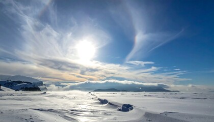 A stunning, vast, wintry landscape under a vibrant blue sky with a halo around the bright sun, with snow-covered ground and wispy clouds