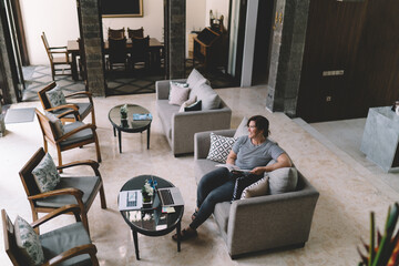 Freelancer relaxing with book in coworking lounge, laptop and charts nearby, balancing digital productivity with mindful offline pause in elegant workspace.