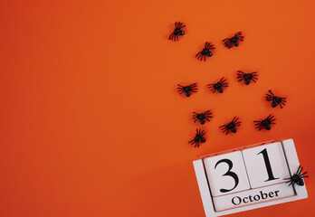 Spooky Halloween flat lay with October 31 calendar and black spiders crawling on orange background. Perfect for eerie holiday designs. 