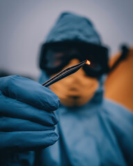Person in Protective Suit Holding Tweezers with a Flame Visible