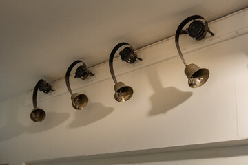 Vintage brass servant bells on curved mounts, once used to summon staff in a historic home, casting striking shadows in a pale hallway.