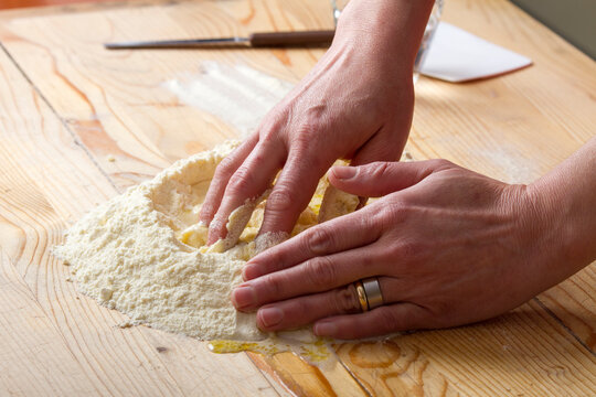 Close-up of a woman's hands kneading dough to make fresh pasta on a wooden chopping board