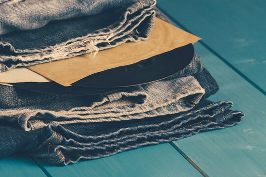 Close-up of two vintage vinyl records in record sleeves in between a stack of folded vintage jeans