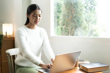 Young Asian woman enjoying a peaceful moment reading a book near window. Calm lifestyle, self-learning, and mindfulness at home.