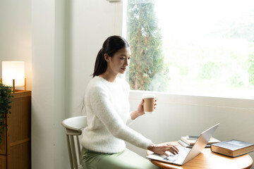 Young Asian woman enjoying a peaceful moment reading a book near window. Calm lifestyle, self-learning, and mindfulness at home.